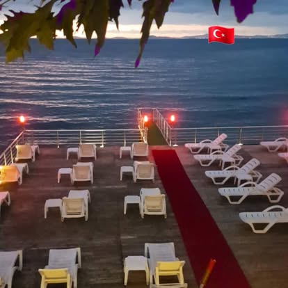 Alacakaranlıkta Çamlık Beach iskele terası; denize bakan şezlonglar ve kırmızı halılı yürüyüş yolu